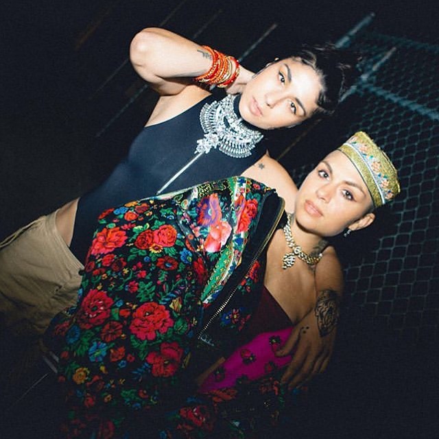 Yasmine Yousaf in a black top and light brown pants posing with her sister Jahan Yousaf in a colorful dress.